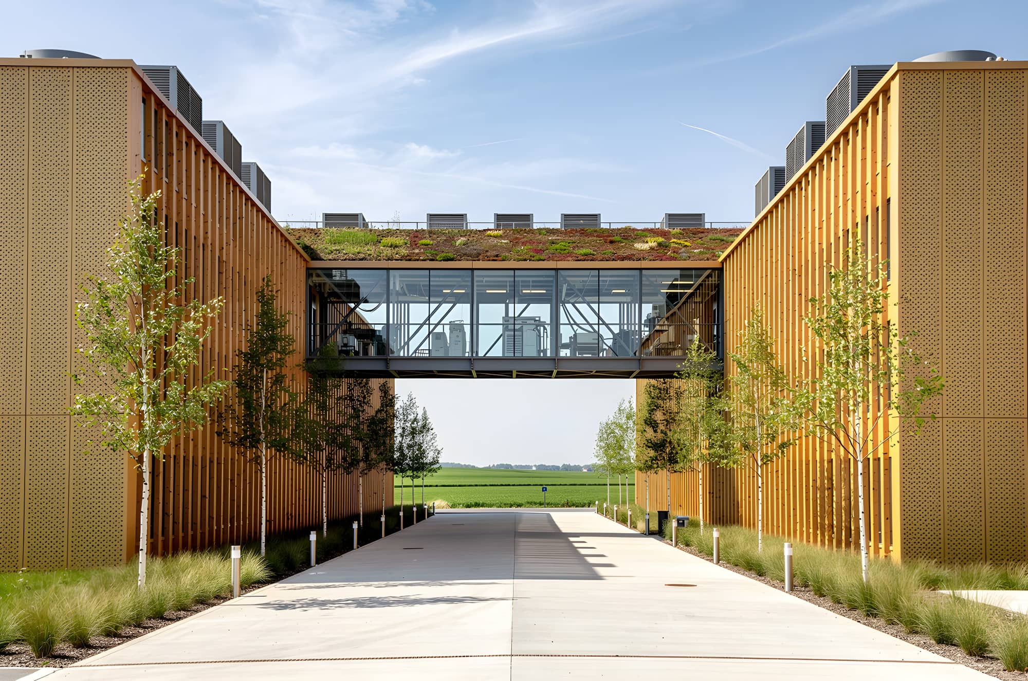 Daylight view along the service street between two data halls, with a glazed link bridge carrying the shared technical spine and planted roofs above